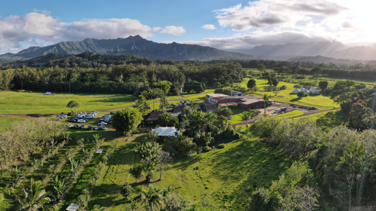 Aerial view of the Food Innovation Center, surrounded by lush green nature. Across the horizon, there is the mountain line and some clouds on a sunny day.