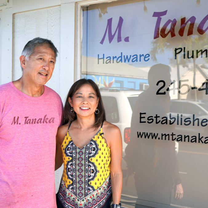 Smiling couple stand at the store front of their hardware and plumbing business.